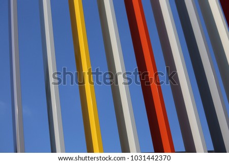 Close up outdoor view of the detail of a colorful gate made of iron bars. Pattern with vertical painted elements with a blue sky in background. Abstract architectural picture. Image with many stripes.