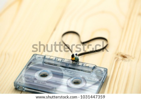 Miniature people : Couple of love sitting on Audio cassette with magnetic tape in shape of heart on wood background.
