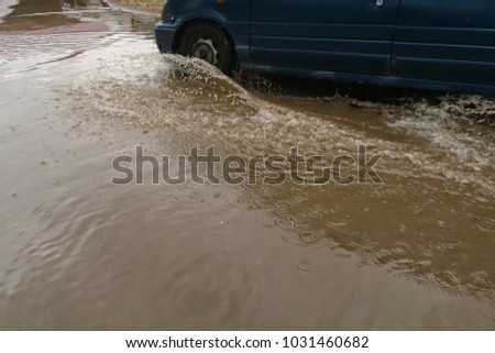 Car splashes trough water on a partly flooded road.

