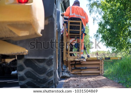 Road construction workers repairing highway road on sunny summer day. Loaders and trucks on newly made asphalt. Heavy machinery working on street. Road curbs being constructed with gravel 