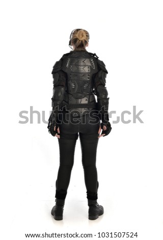 full length portrait of female wearing black  tactical armour, standing pose with back to the camera, isolated on white studio background.