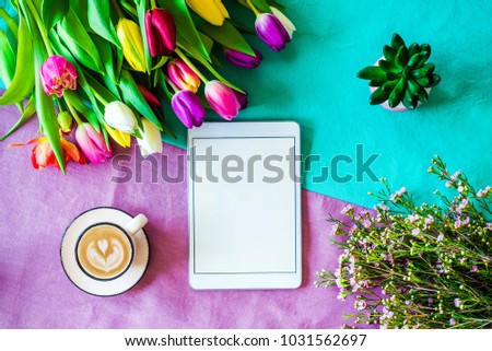 Happy Easter spring shot from above as flatlay with blank tablet screen for message and colorful tulips, flowers and coffee cup