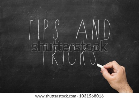 Hand with chalk writing Tips and Tricks concept on black chalkboard.