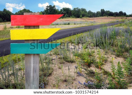 Wooden sign (blank) in red, yellow and green. Background landscape with a road. 