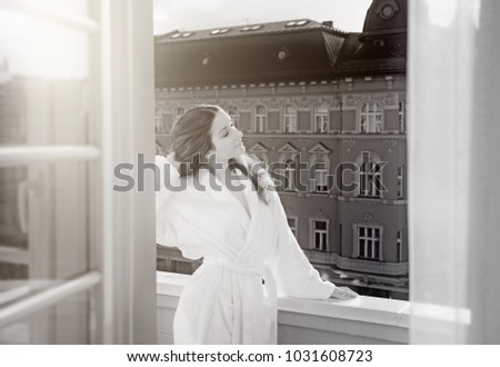 Beautiful woman at morning wearing robe standing on the balcony overlooking old European streets. Concept of beautiful life, relax or vacation