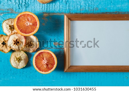 wooden photo frame on blue wooden surface texture with empty place for text or image with slices of dried apple, red orange