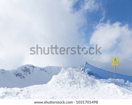 A lot of snow in the mountains and a blue grid and a yellow sign warning tourists about the danger in the mountains in Sochi, Russia
