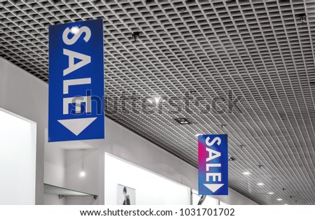 two rows of vertical sale posters with white letters hang from grid ceiling in big shop in sale season.