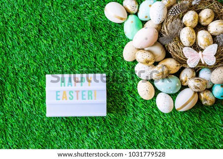Shot from above as flatlay with happy easter message written on light box and colorful retro easter eggs, grass, butterfly and easter nest 
