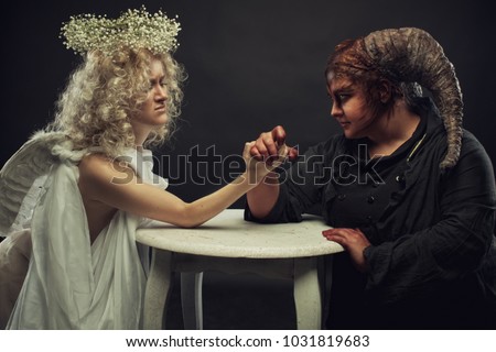 Demon and angel have  competition at arm wrestling on a table