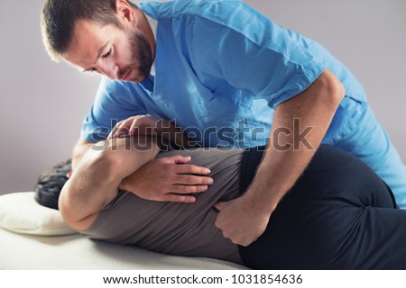 Physiotherapist doing healing treatment on man's back. Therapist wearing blue uniform. Osteopathy. Chiropractic adjustment, patient lying on massage table Royalty-Free Stock Photo #1031854636