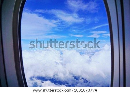 Airplane window view with blue sky and white clouds.