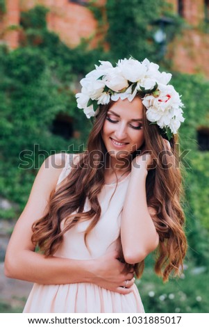 Happy girl with long hair in a wreath of peonies, green wall on background