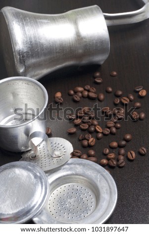 The Vietnamese teapot for coffee in disassembled form and cezve lies on a dark surface. Next scattered coffee beans.