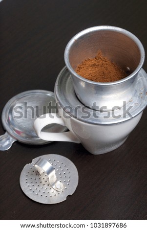 Vietnamese coffee maker is equipped on a cup. Ground coffee is poured into it. Nearby lie the rest of the brewer.