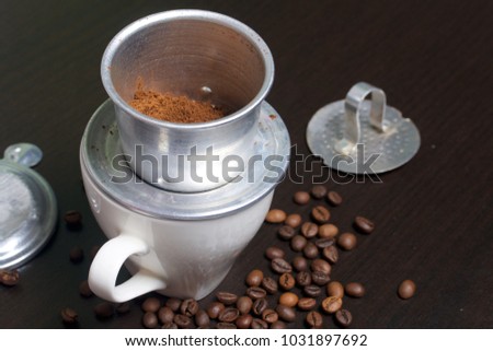 Vietnamese coffee maker is equipped on a cup. Ground coffee is poured into it. Nearby lie the rest of the brewer.