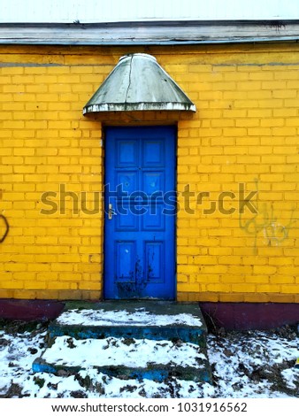 Dilapidated bright yellow brick house with blue door and steps in front of it in winter