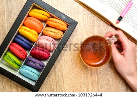 Macarons, a book, a cup of tea, a woman's hand. Macarons for breakfast.