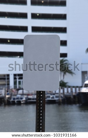 Rectangular blank white sign with water boats and a parking garage in background