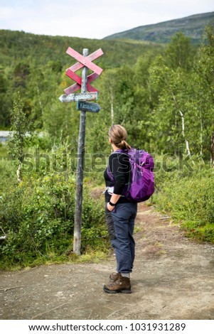 Female with backpack looking at a sign at the walking trail of Kungsleden in Lapland, Sweden.