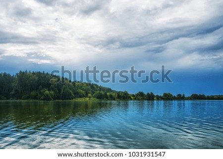 The shore of a forest lake is reflected in water, the sky with clouds above it.