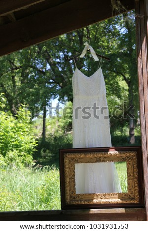 Getting ready for the wedding.  Antique picture frame on a ledge of the shelter with the white wedding dress hanging draping behind.  The lush greenery and blue sky make a nice backdrop.  2017