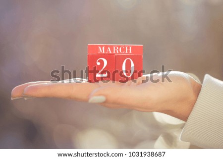 the woman is holding a red wooden calendar. Red wooden cube shape calendar for MARCH 20 with hand 