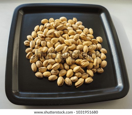 Pistachio nuts, a bunch on a black plate. A close-up photograph. Unrefined whole kernel