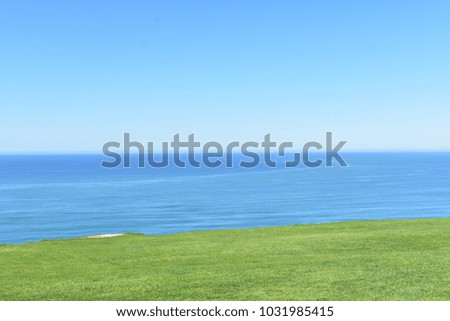 A picture great for background showing an outdoor view of a sunny day in summers with a blue sky, blue ocean water and green grass in equal proportions.