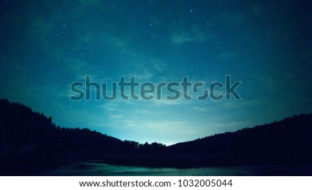 Lake at night - timelapse. Video. Night sky timelapse with running stars. A view of the stars of the Milky Way with a silhouette of a pine trees forest near a lake in the mountain. Falling stars