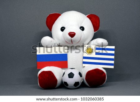 Teddy bear holding Russia and Uruguay Flag with a football