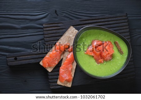 Cream-soup with green peas topped with salmon fillet, view from above on a black wooden background, studio shot