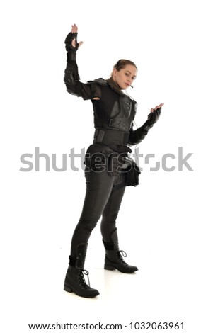 full length portrait of female  soldier wearing black  tactical armour and headset standing pose  with arms raised, isolated on white studio background.