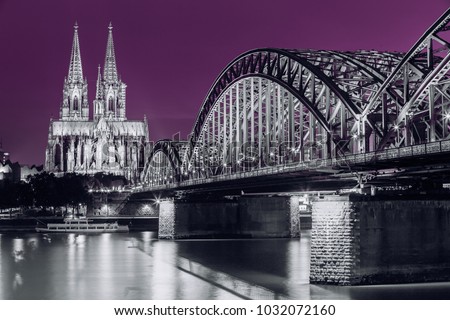 Cologne, Germany. Night View Of Cologne Cathedral And Hohenzollern Bridge. Catholic Gothic Cathedral In Night Lighting.  UNESCO World Heritage Site. Black, White And Ultra Violet Colors