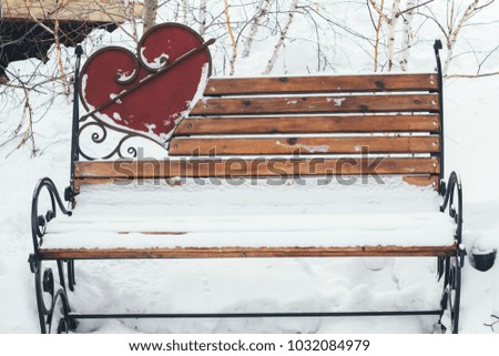Snow-covered bench in the park with a heart shaped decoration
