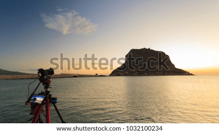 Professional camera on tripod taking picture film video from Monemvasia island at sunrise over sea surface, Greece Peloponnese Lakonia