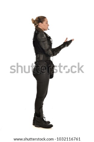 full length portrait of female  soldier wearing black  tactical armour and headset standing side profile, isolated on white studio background.