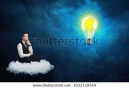Caucasian businessman sitting on a white fluffy cloud lookind and wondering at a big, shiny, glowing yellow lightbulb