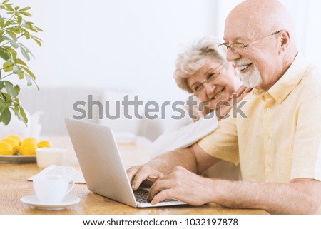 Smiling elderly man and his wife searching for information on the internet using laptop