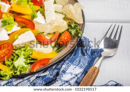 Salad with cheese and fresh vegetables on white wooden table.