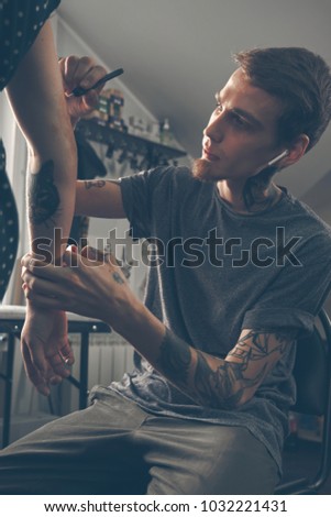 A young guy, a tattoo artist preparing for the session, draws a sketch on the body of the client in a welcoming environment