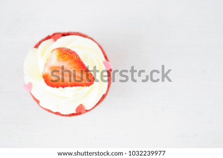 Cupcakes red velvet with white whipped cream decorated with strawberry and confectionery sprinkles in form of heart on white wood table. Picture for a menu or a confectionery catalog.