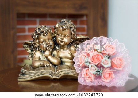 Wedding bouquet next to the angels and fireplace. The bouquet of the bride lies on the table next to the sculpture of two little angels reading the book.