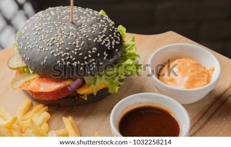 Black burger on a wooden background with potatoes and sauce