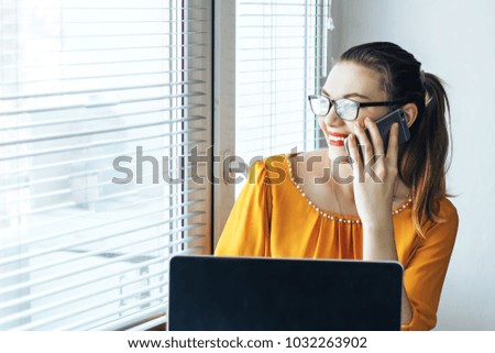smiling girl in glasses talking on phone near computer