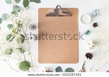 Flat lay top view photo of a clipboard on a white wooden background with gentle flowers and plants. Cute feminine mock up. Blank space.