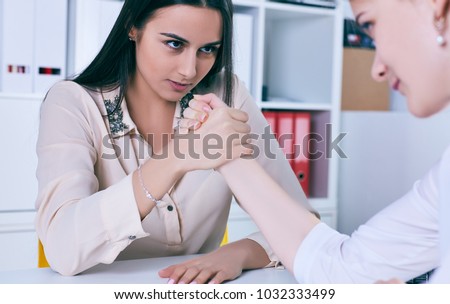 Two female office wokers armwrestling, exerting pressure on each other, struggling for leadership.