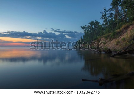 The steep sandy shore of the river at sunset. Summer, warm evening. Fallen trees in the water.