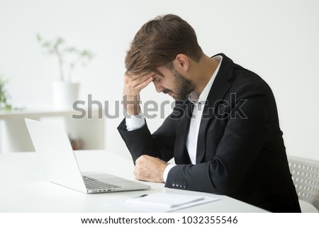 Depressed unsuccessful businessman feels terrible headache, distraught stressed entrepreneur regrets of business mistake shocked by bankruptcy desperate after failure sitting at work desk with laptop Royalty-Free Stock Photo #1032355546