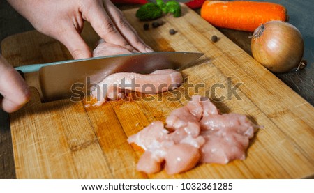 Cook chef hands woman cuts raw chicken breast on a wooden background.
